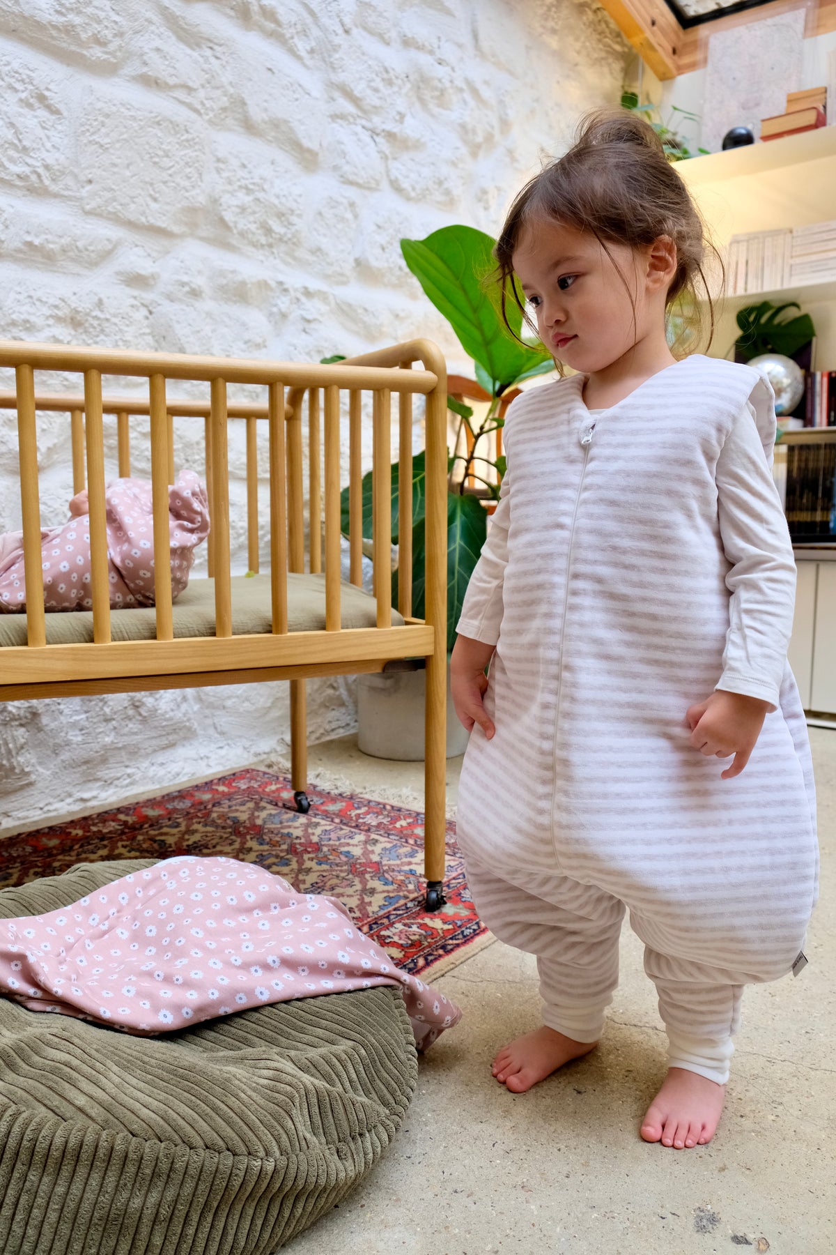 petite fille debout avec une gigoteuse à pieds et un lit à barreau derrière