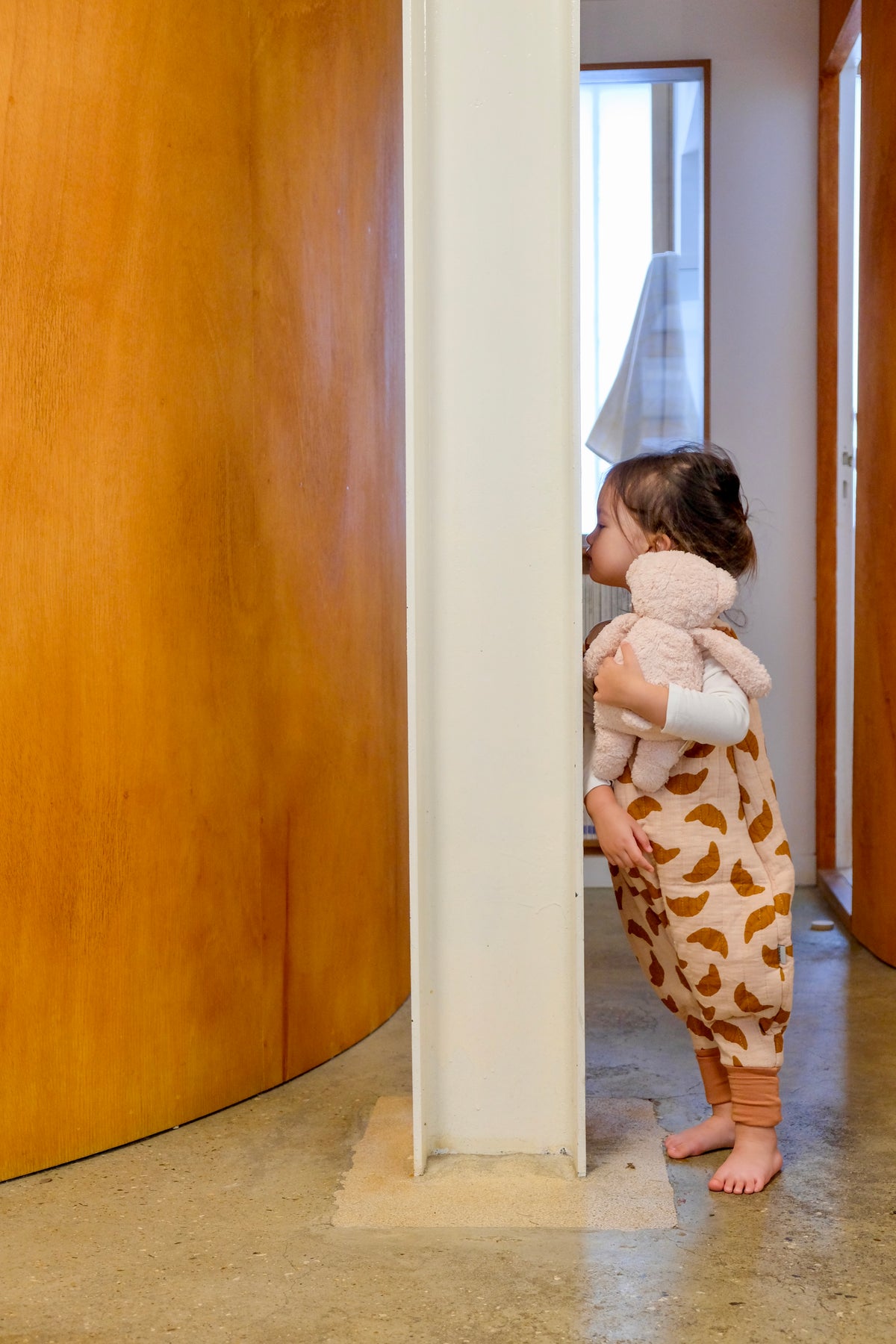 enfant embrassant le mur avec peluche dans les bras et portant une gigoteuse à pieds croissant